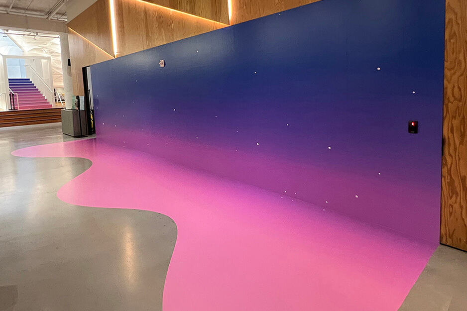 Pink to indigo graphics covering a wall and continuing onto the floor in curving pattern.